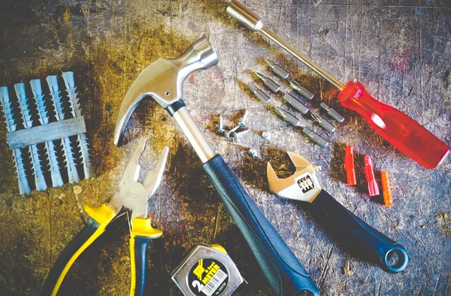 Hammer, Zange, Schraubenschlüssel, Schraubendreher und Dübel liegen auf einer Werkbank bereit.