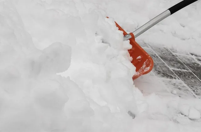 Rote Schneeschaufel schiebt frischen Schnee von einem gepflasterten Weg.
